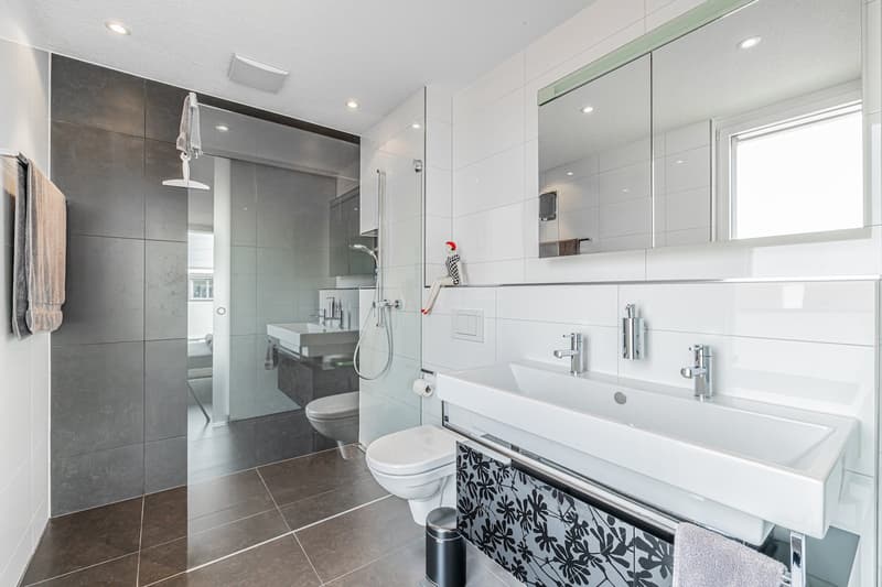 modern bathroom with white tiles, double sink, shower, toilet, towel rack, mirror