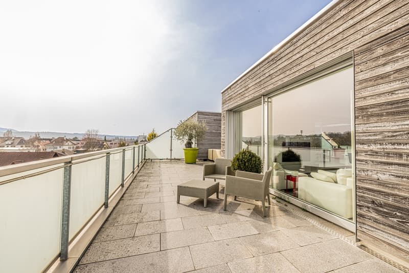 Balcony with glass railing, wooden wall, outdoor seating, potted plants, city view