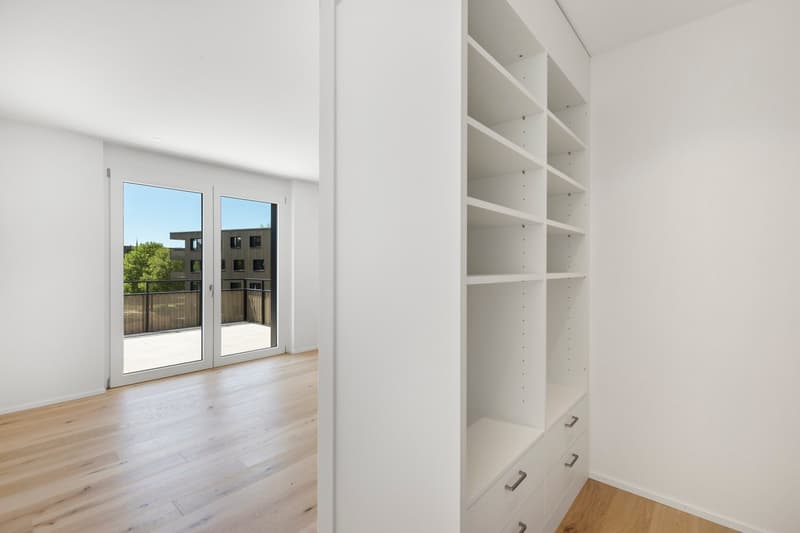 Spacious bedroom with large windows, hardwood flooring, and built-in shelving units along the wall.