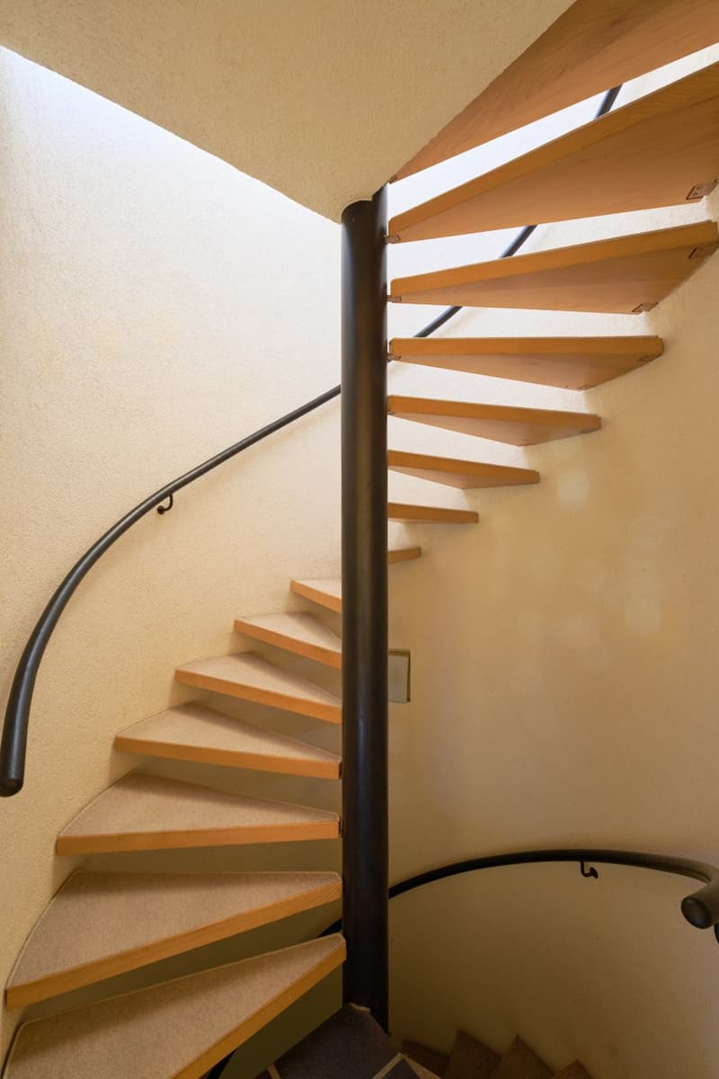Spiral staircase with wooden steps and a black metal railing, leading up to a higher level.