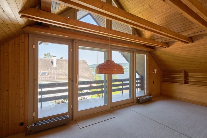 Spacious living room with wooden beamed ceiling, large windows overlooking a balcony or terrace, and a pendant light fixture.