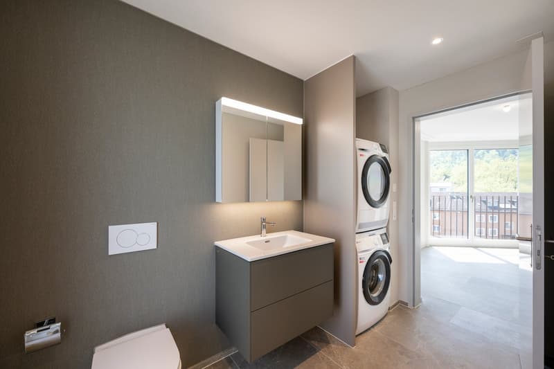 A bathroom featuring a white toilet, a sink, a mirrored cabinet, and an in-unit washing machine