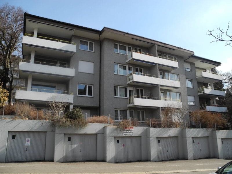 multi-story apartment building with balconies, grey exterior, multiple garages