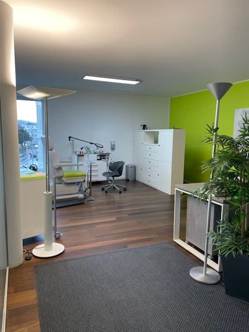 modern office room with wooden floor, white walls, green accent wall, white furniture, office chair, desk, lamp, potted plant