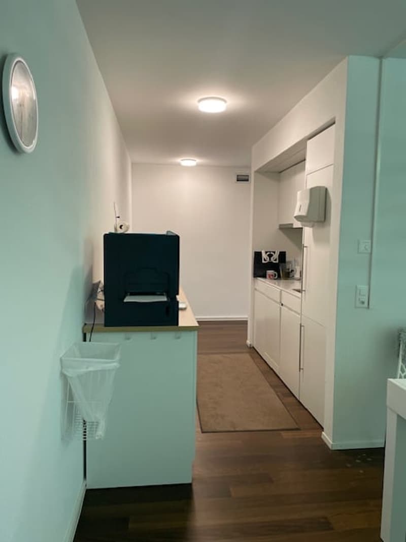 small kitchen with a printer, a rug, a clock, and a trash bin
