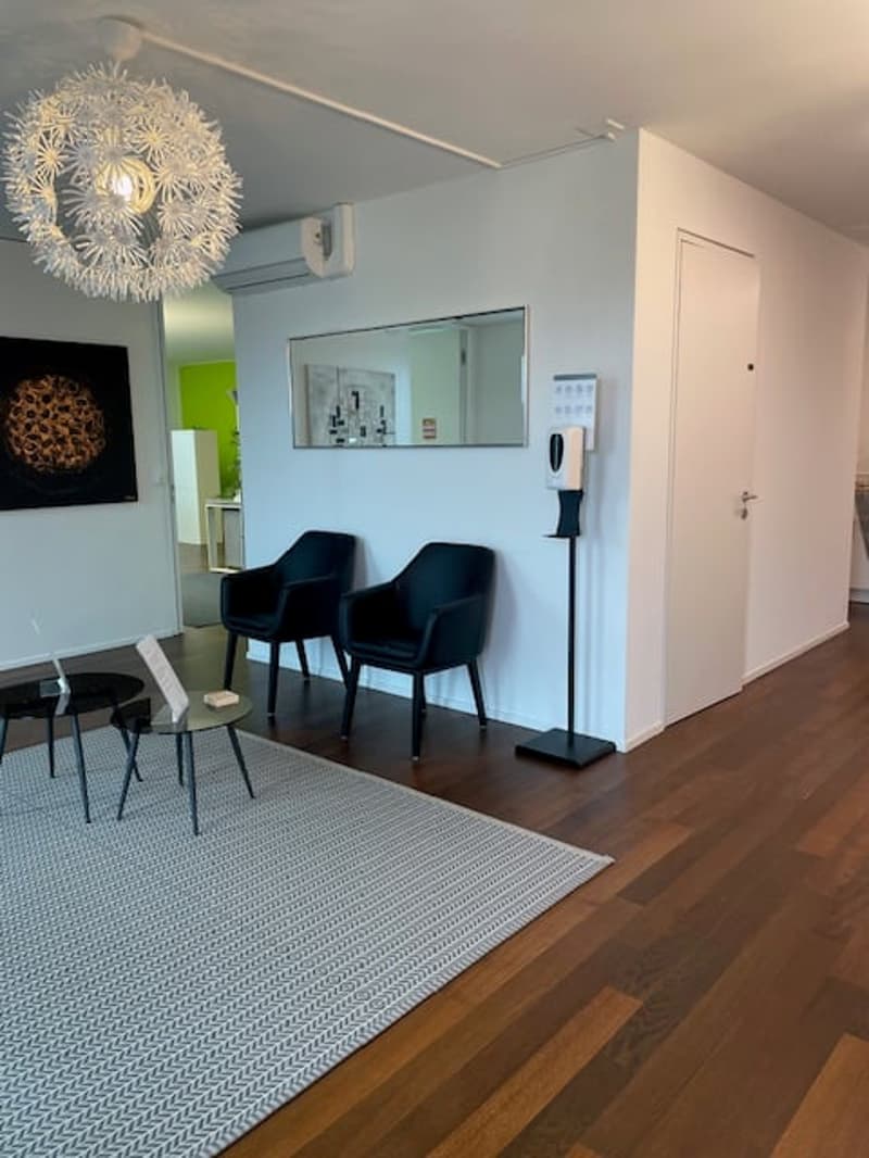 modern room with wooden floor, white walls, black chairs, round table, chandelier, mirror, hand sanitizer