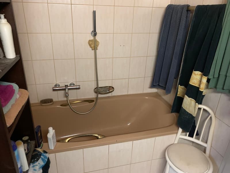 Bathtub, towels, toiletries, shelf, chair, tiled walls, silver showerhead