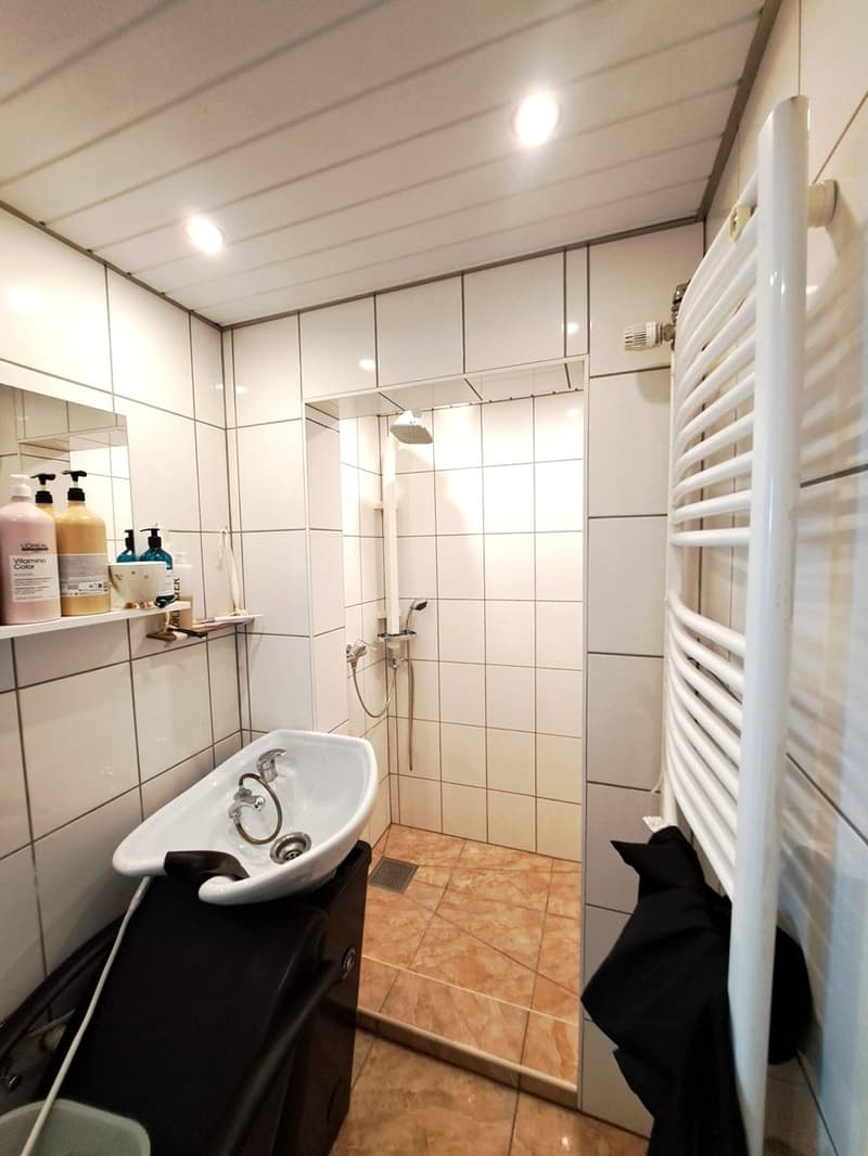 White walls and tiles, a white sink with faucet and drain, a shower with a handheld showerhead, a mirror, and a towel rack