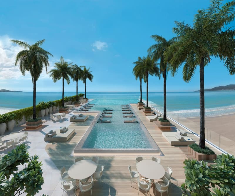 Outdoor area with swimming pool, lounge chairs, tables, and palm trees, overlooking the ocean.