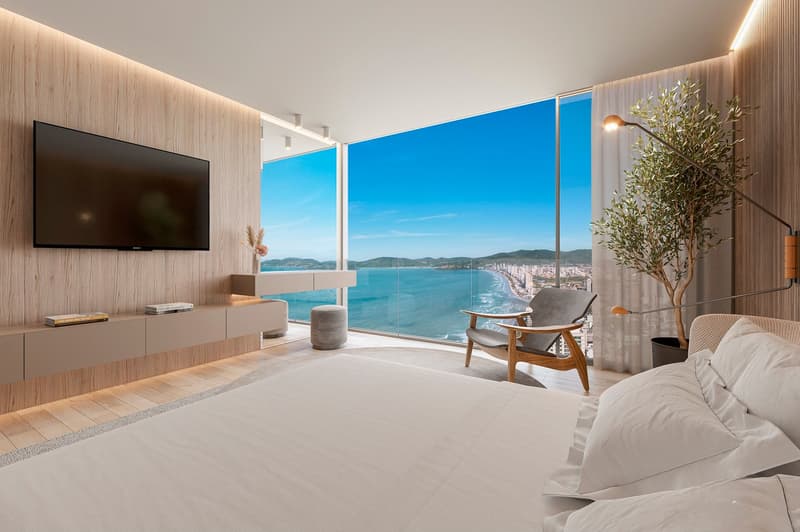 modern bedroom with large bed, wooden floor, large windows, TV, wooden chair, desk, plant, view of the sea