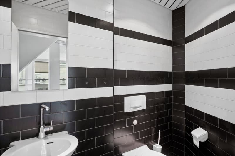Bathroom with black and white tile walls, a sink with a faucet, and a toilet.