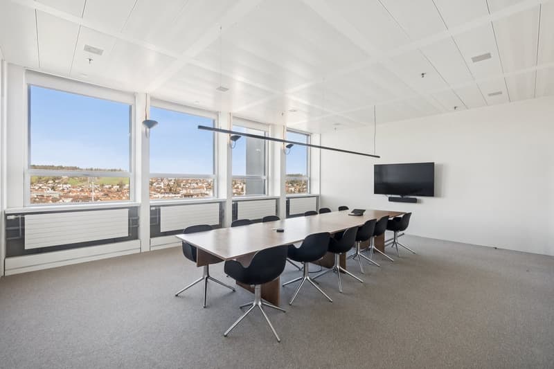 empty conference room with large windows, long table, black chairs, mounted TV