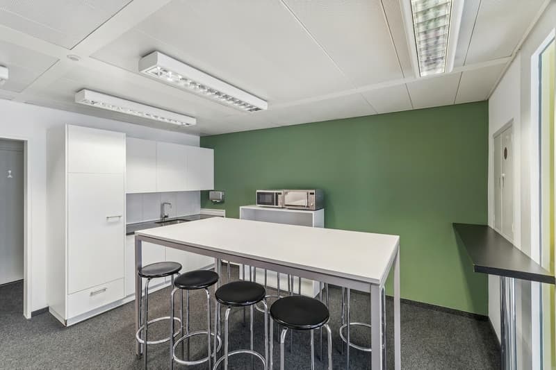 modern kitchen area with white countertops, black stools, green wall, white cabinets, microwave, sink, faucet