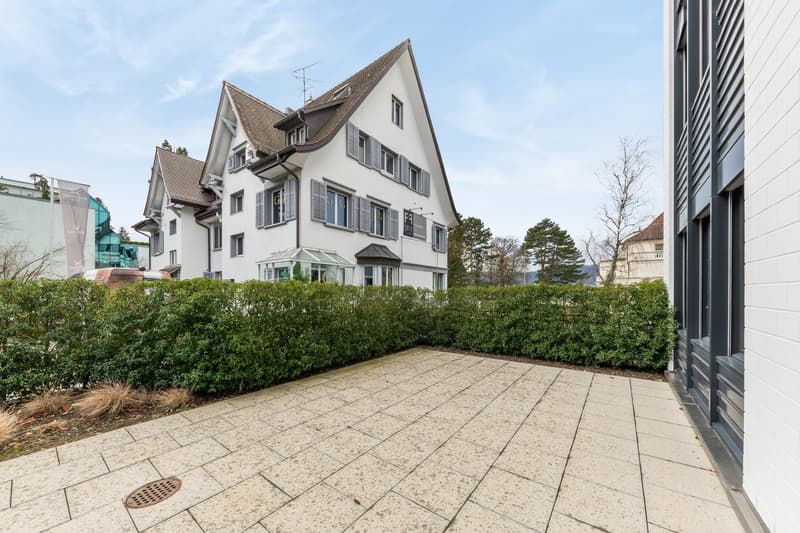 white house, brown roof, multiple windows, hedges, paved courtyard