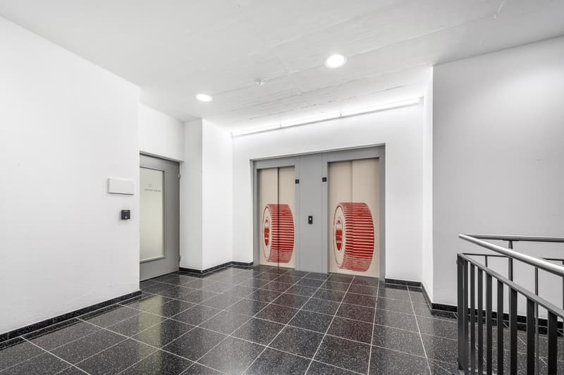 elevator room, white walls, black tiled floor, two elevators with red tire designs