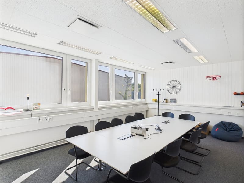 Large conference room with white walls, large windows, white table, black chairs, and various office equipment and decor
