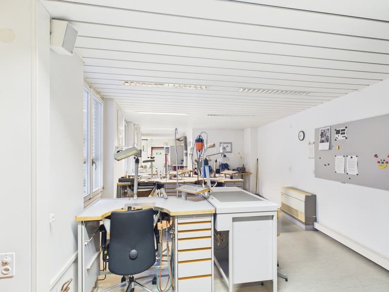 Empty office space with desks, lamps, office chairs, wall mounted bulletin board and clock