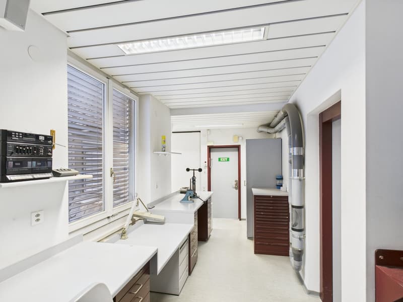 office-like room, white walls, wooden cabinets, work tables, shelves, electronic equipment, large window, exit door, ceiling with lights