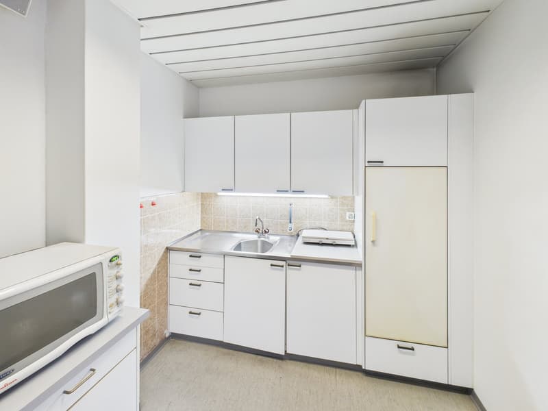 Compact modern kitchen, stainless steel countertop, sink, gas stove, refrigerator, white cabinets, microwave on counter