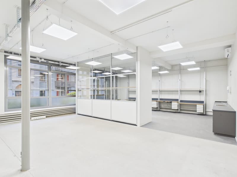 Empty room with office furniture, large windows, bright white lighting, white ceiling and walls, glass partitions, gray countertop.