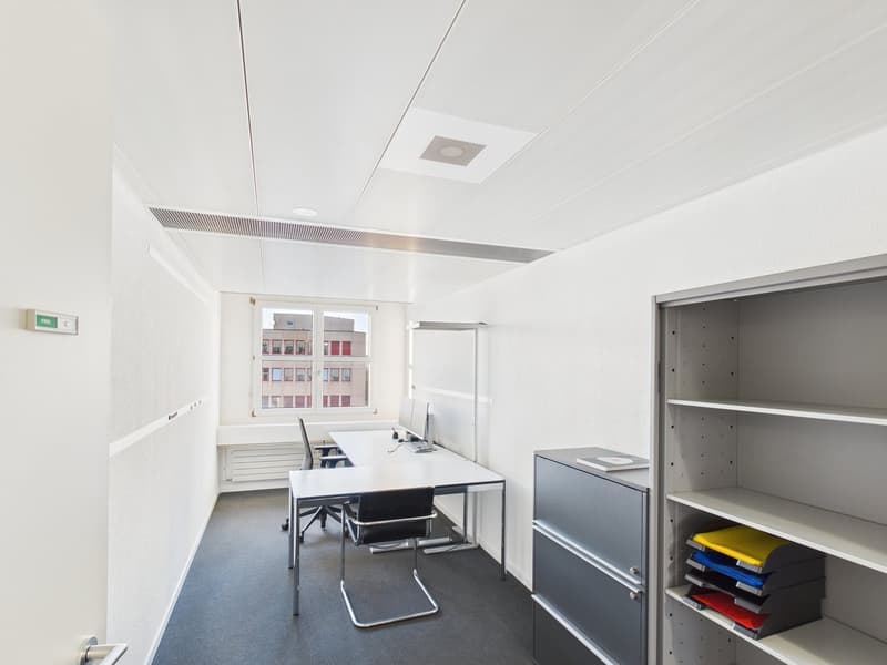 Empty room with white desk and chairs, glass windows, gray filing cabinet, shelves with office supplies, ceiling with ventilation system