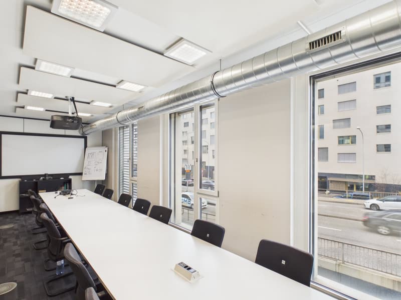 conference room with large table, chairs, projector, whiteboard, glass windows, view of outside road