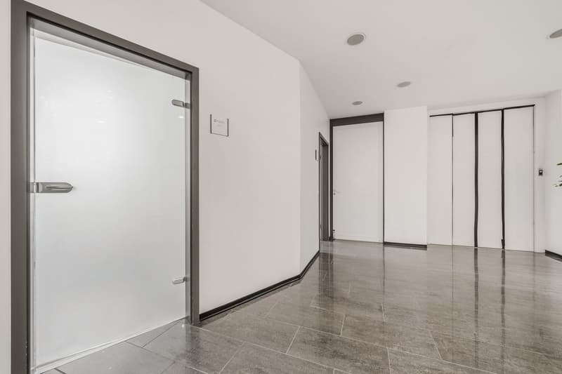 Empty room with white walls, gray tiled floor, two doors, one with a silver handle, and a sign on the wall.
