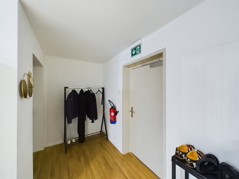 An empty hallway with a clothes rack, fire extinguisher, and shoes on a table