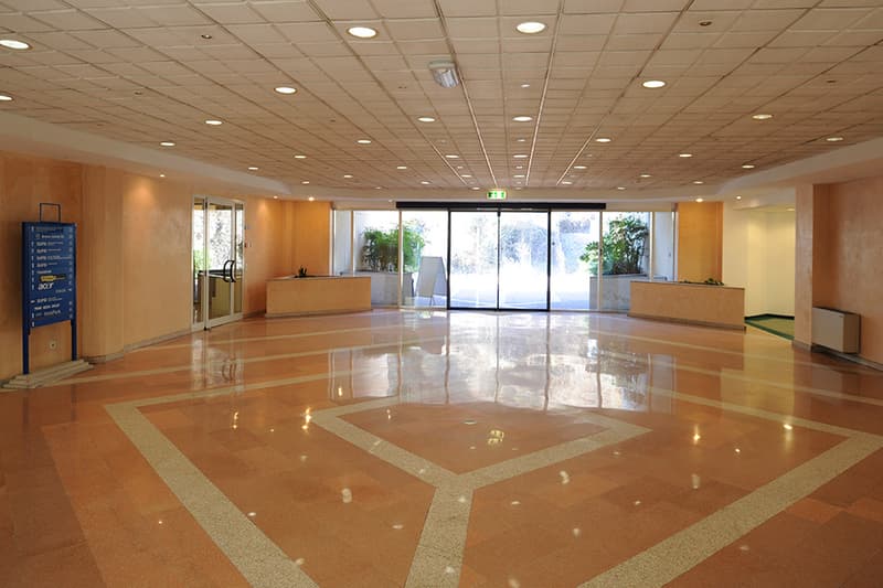 An empty building lobby with high ceilings, tiled floor, and double glass doors