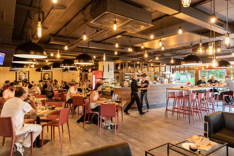 restaurant interior with wood floors, red chairs and tables, hanging lamps, a bar, and customers