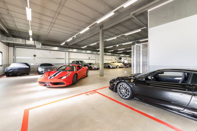 Spacious underground garage, multiple sports cars parked, fluorescent lighting, numbered parking spots
