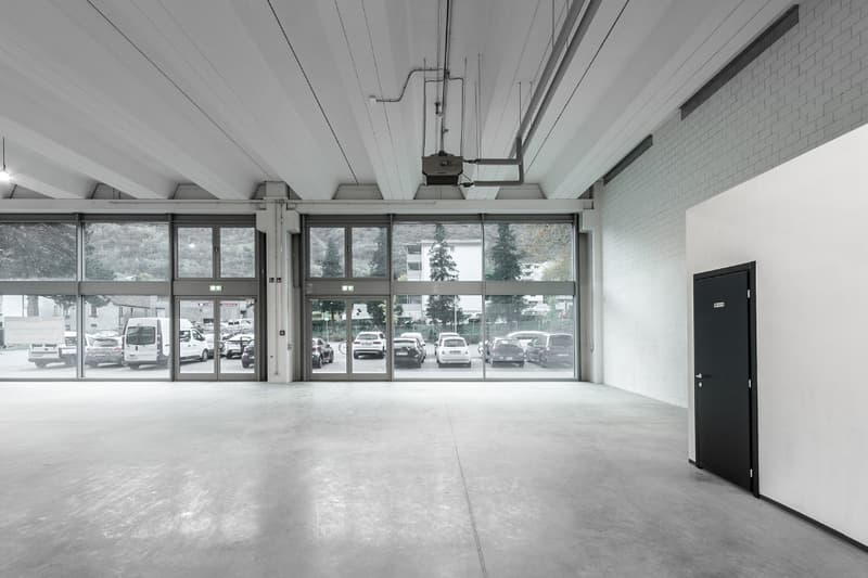 open room, gray floor, large windows, black door, vehicles parked outside