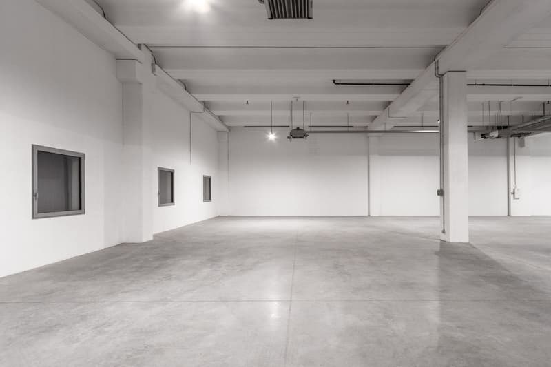 The room is completely empty with concrete floors, white walls and ceilings, and multiple small windows.
