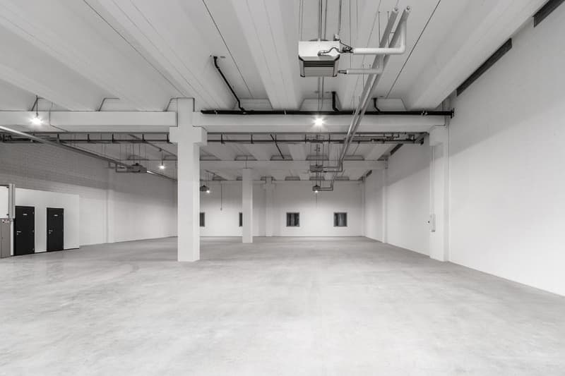 Empty room, concrete floor, white walls, black industrial style ceilings and beams, small windows, doors on the left side, spotlights