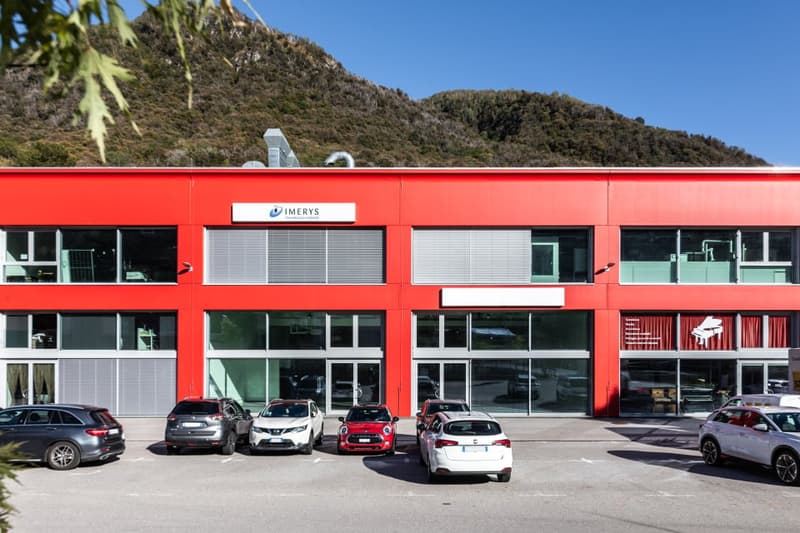 A modern, red building with a large entrance, glass doors, windows, and multiple cars parked in front