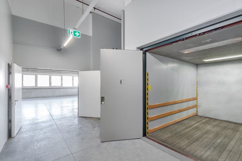 empty large room, with large doors, a white wall, an open door, windows, and a hanging light