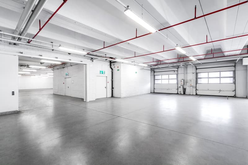 Empty parking garage, concrete floor, fluorescent lighting, garage doors, and walls