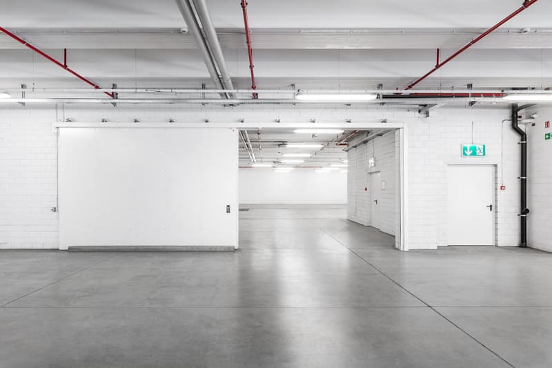 large underground parking space, concrete flooring, white walls, exit signs, emergency lights