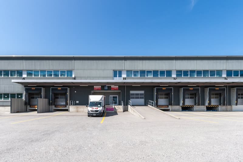 A warehouse-type building with several large doors in the front and several windows, parking lot in front