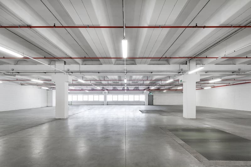 Empty parking lot with concrete floor, white walls, white ceiling, and mounted ceiling lights.