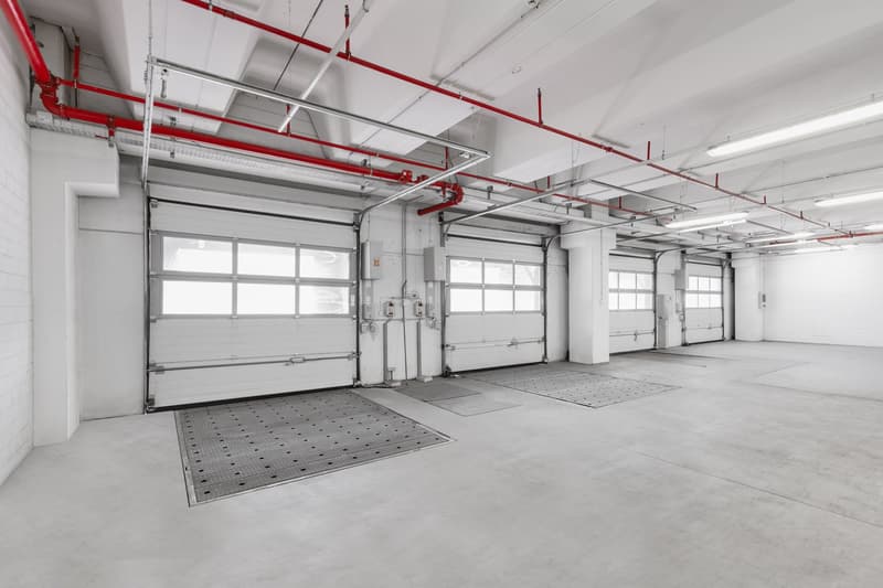 Empty garage with gray concrete floor, white walls, overhead pipes, and three garage doors