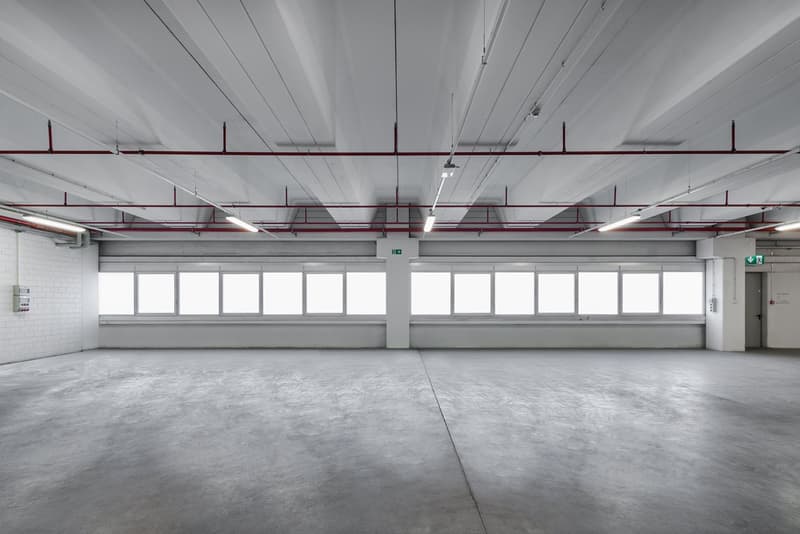 Empty room with grey concrete floor, white ceiling, two rows of windows and red metal supports