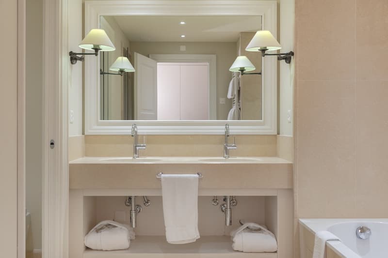 Modern bathroom with a large mirror, two sinks, towel racks, and a bathtub.
