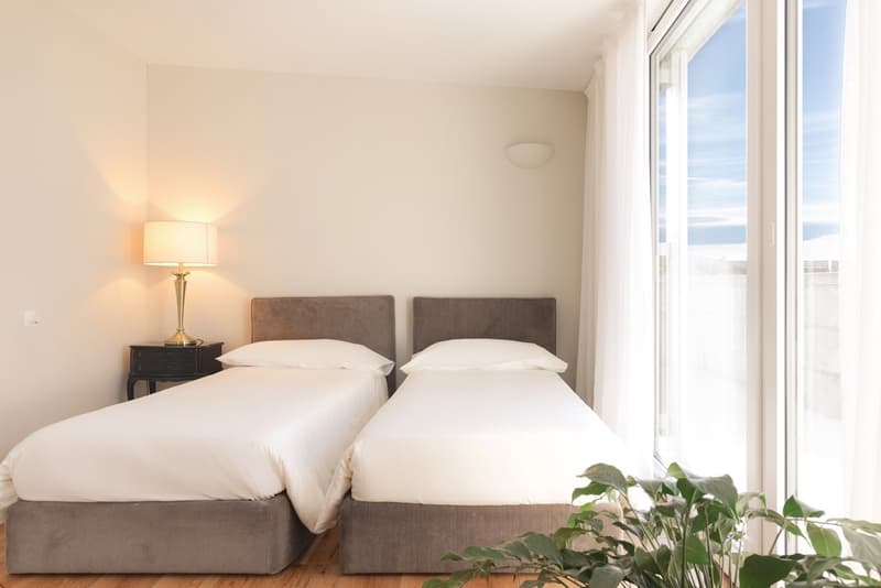 Two beds, bedside tables, floor lamp, large windows, curtains