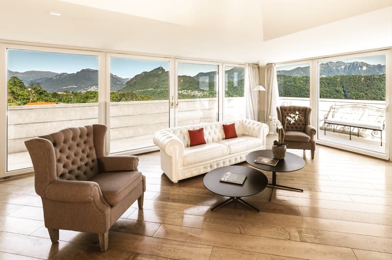 Wooden floor, modern couch, two armchairs, center table, large windows with balcony, vase with flowers