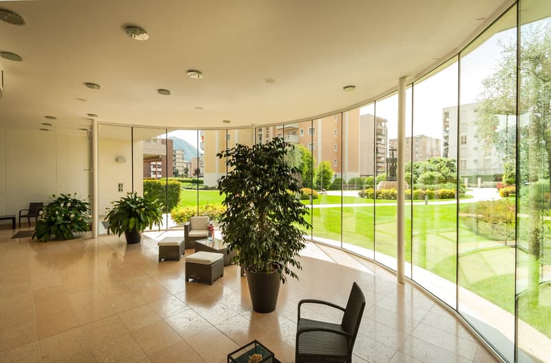 Spacious lobby with large windows overlooking a lush green garden, potted plants, and comfortable seating areas