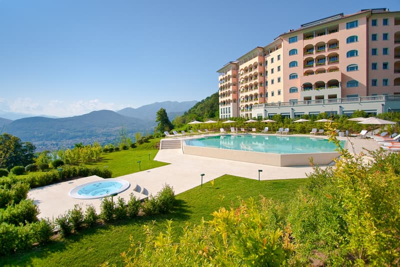 modern building with multiple balconies, large swimming pool, landscaped garden, sun loungers, umbrellas
