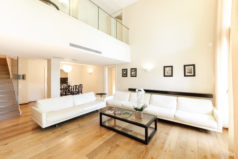 white couches, glass coffee table, white walls, wooden floor, two picture frames, balcony, wooden stairs