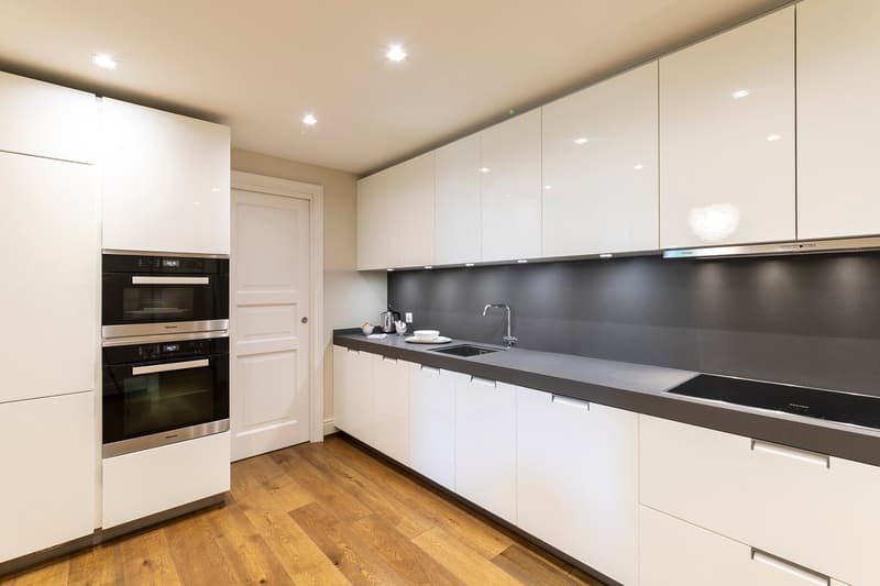 modern open kitchen, white cabinetry, black countertops, stainless steel double oven, sink, induction stove, extractor