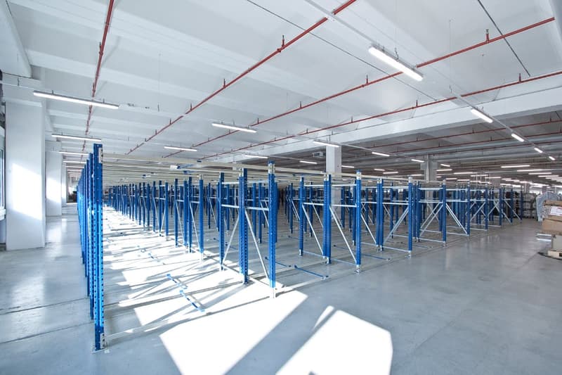 Large industrial warehouse space with rows of blue metal shelving units and overhead lighting